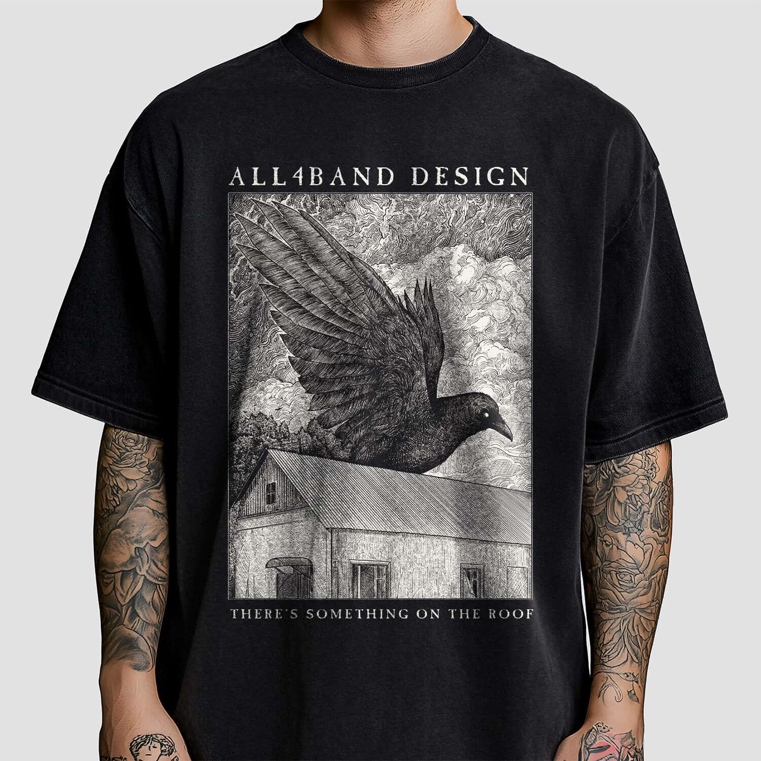 Detailed black and white shirt design featuring a giant raven flying over a rural house beneath dense swirling clouds.
