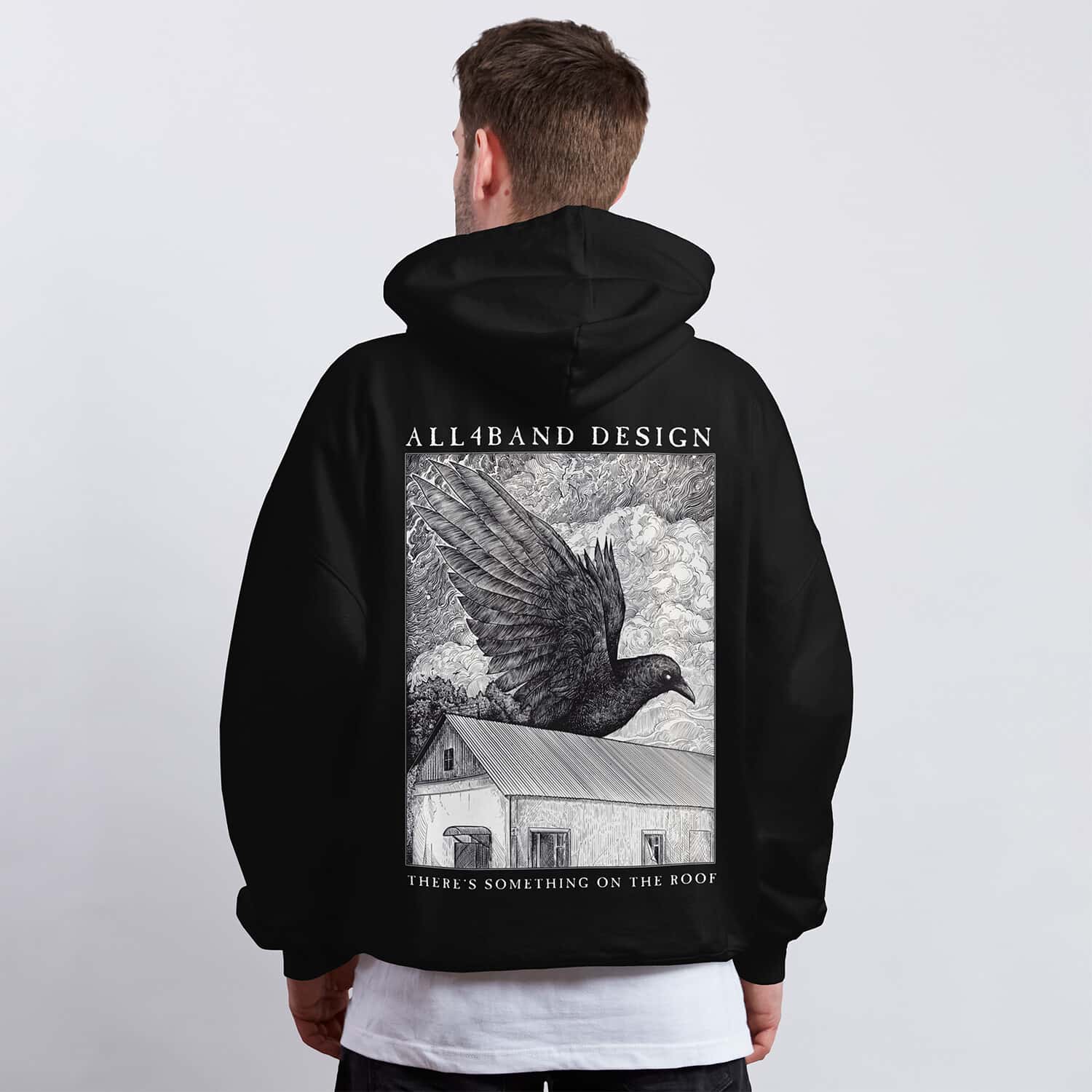 Detailed black and white hoodie design featuring a giant raven flying over a rural house beneath dense swirling clouds.