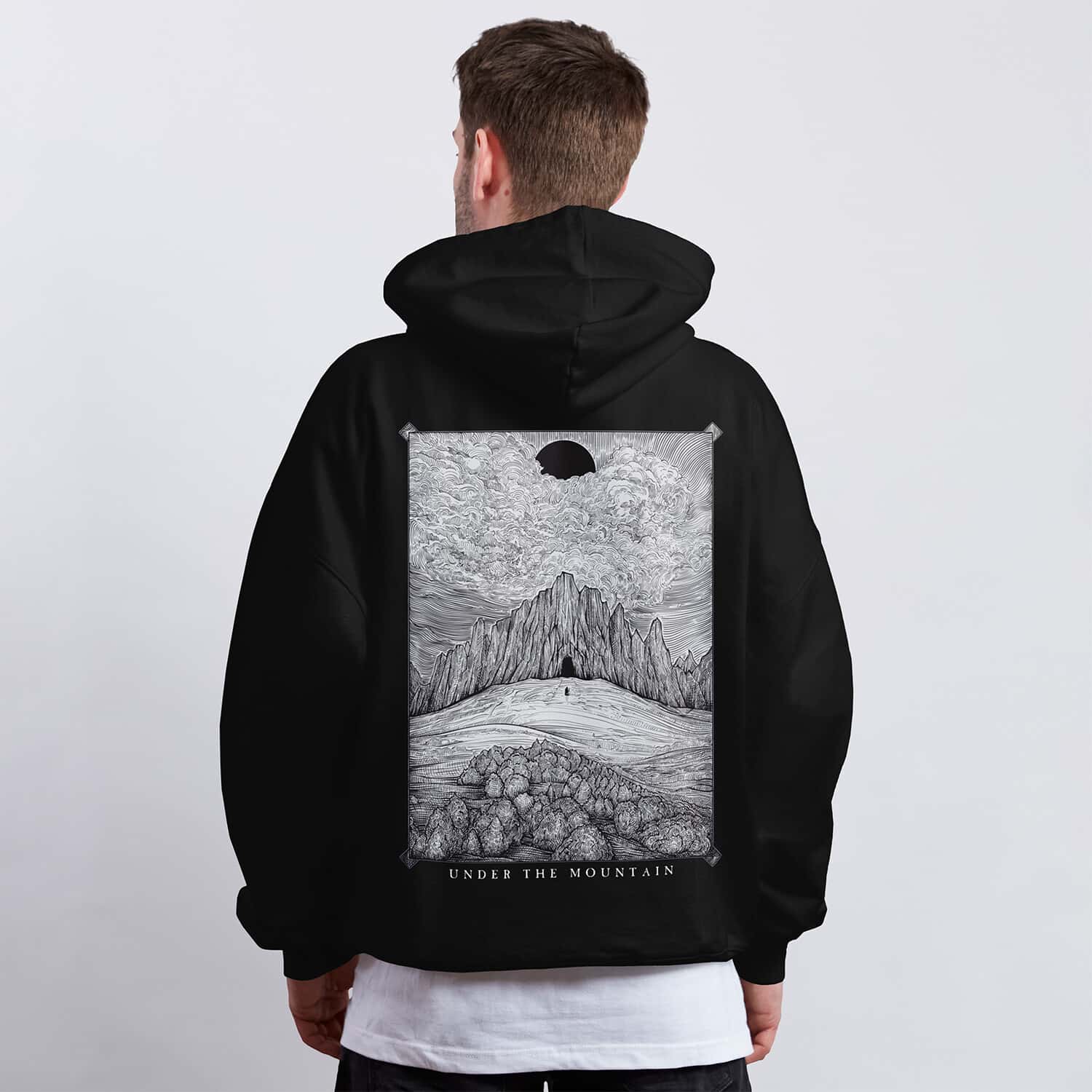 Black and white hoodie design featuring a lone figure approaching a dark mountain beneath a black sun and dramatic clouds.