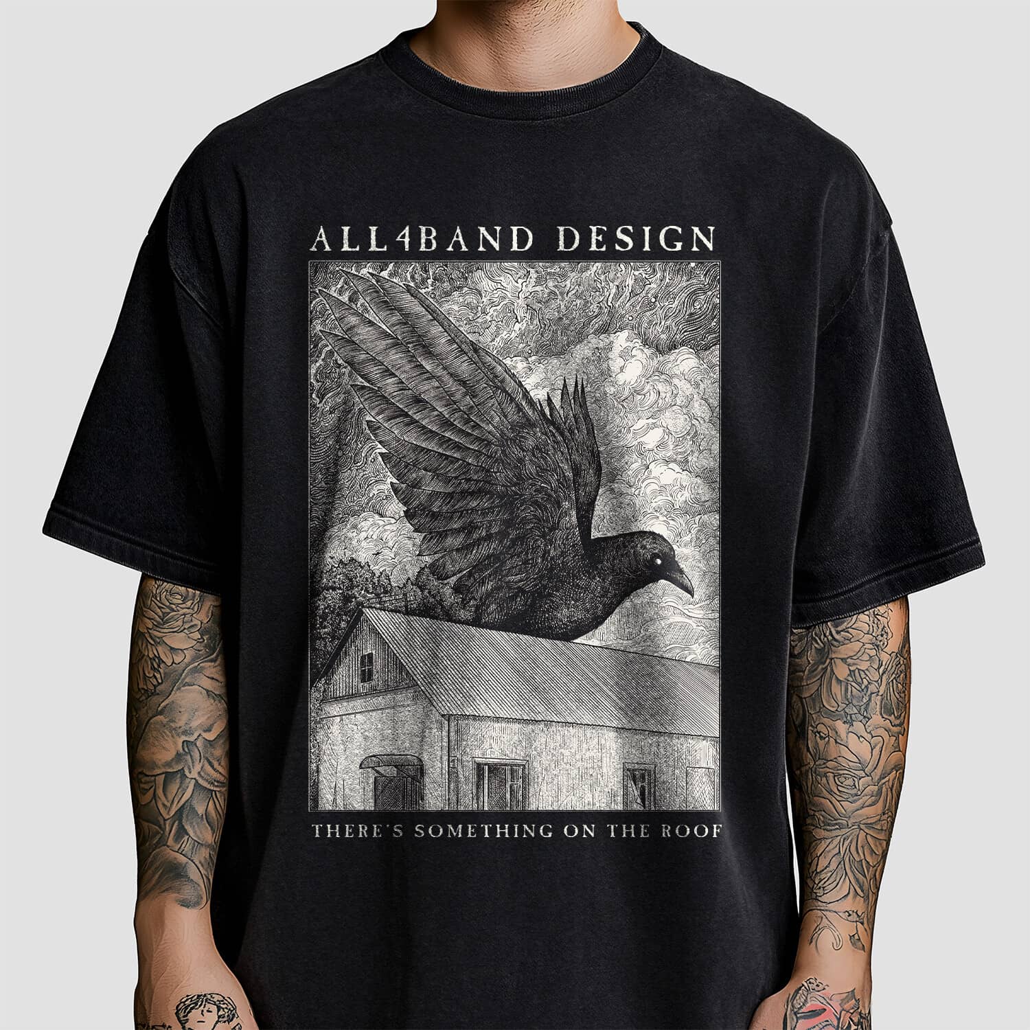 Detailed black and white shirt design featuring a giant raven flying over a rural house beneath dense swirling clouds.