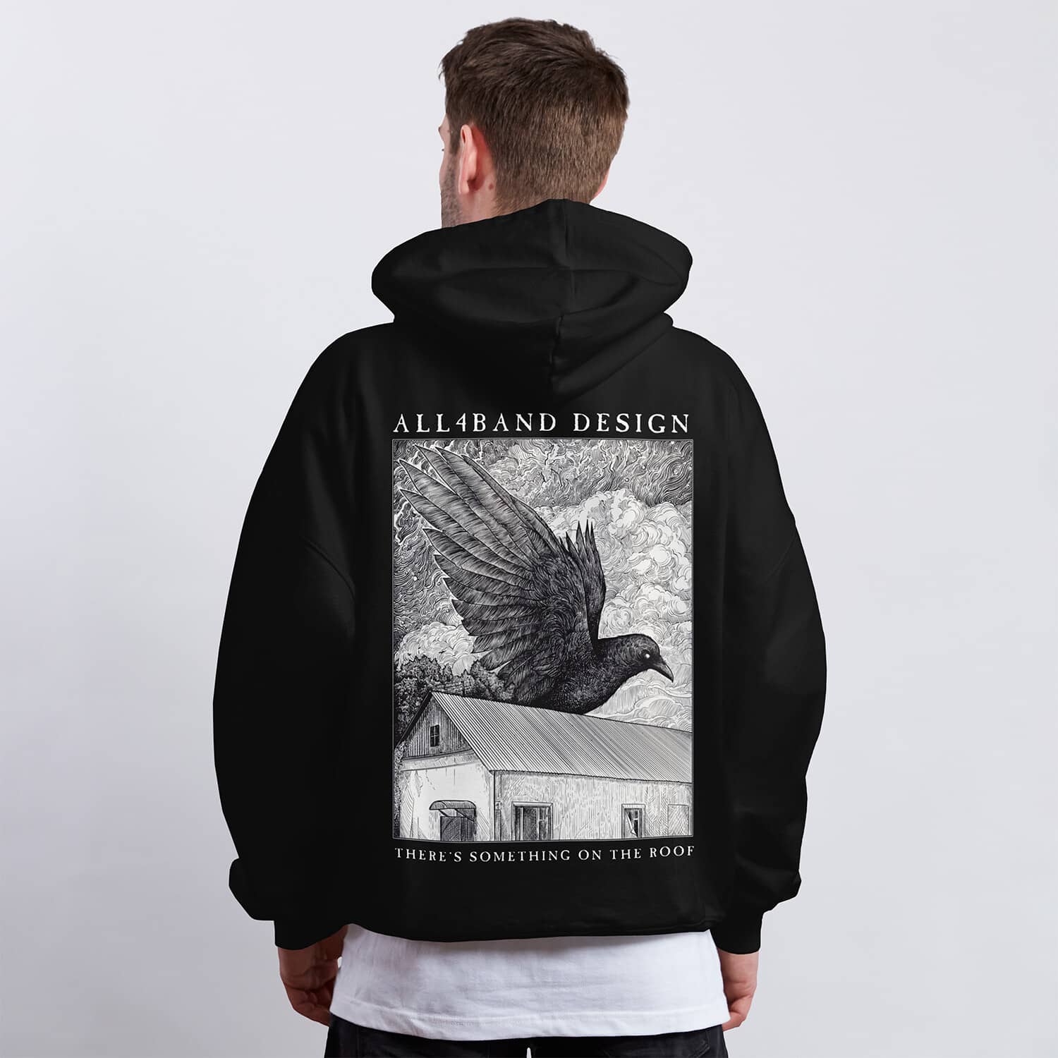 Detailed black and white hoodie design featuring a giant raven flying over a rural house beneath dense swirling clouds.