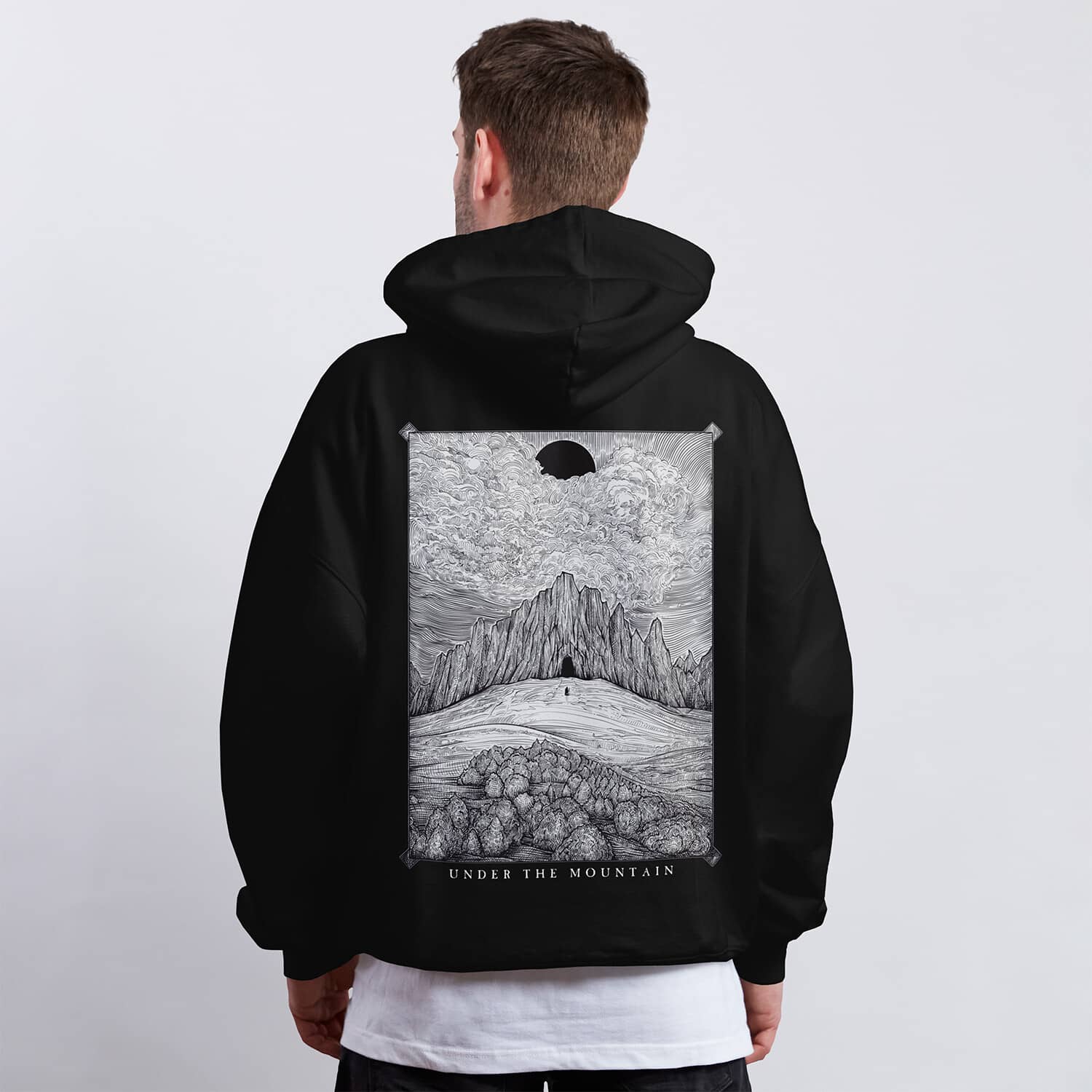Black and white hoodie design featuring a lone figure approaching a dark mountain beneath a black sun and dramatic clouds.